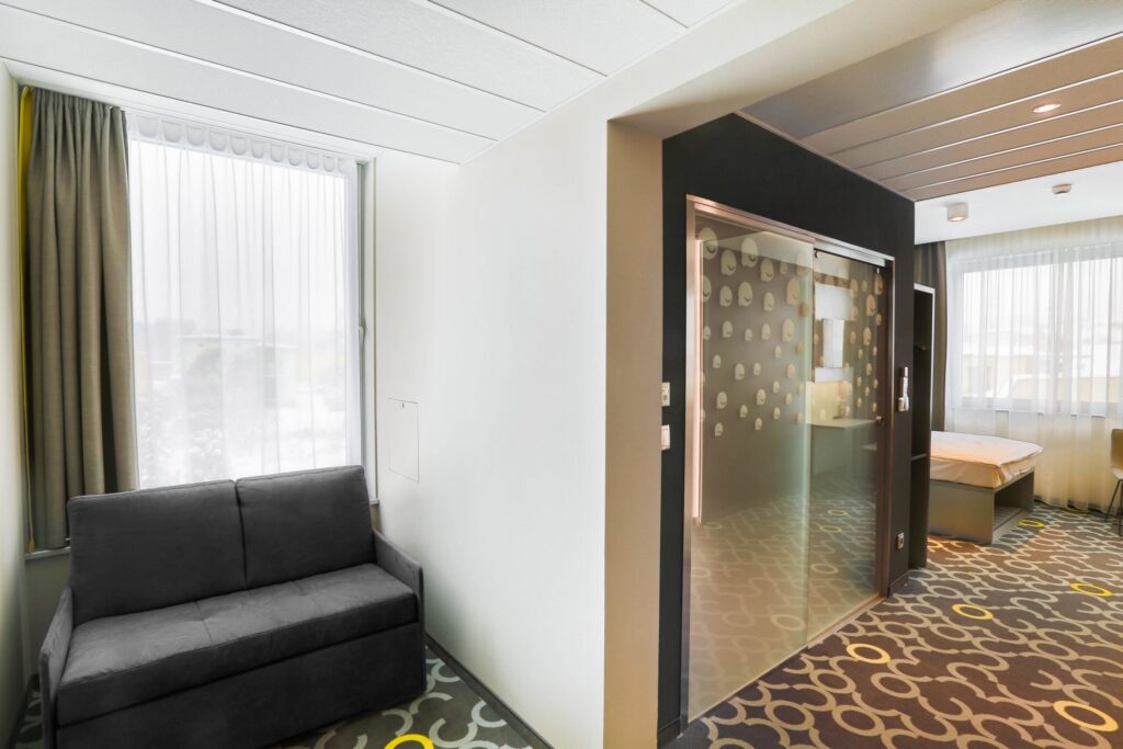 Zdjęcia hotelu – jasny pokój hotelowy z sofą, oknem i przeszklonym wejściem do łazienki